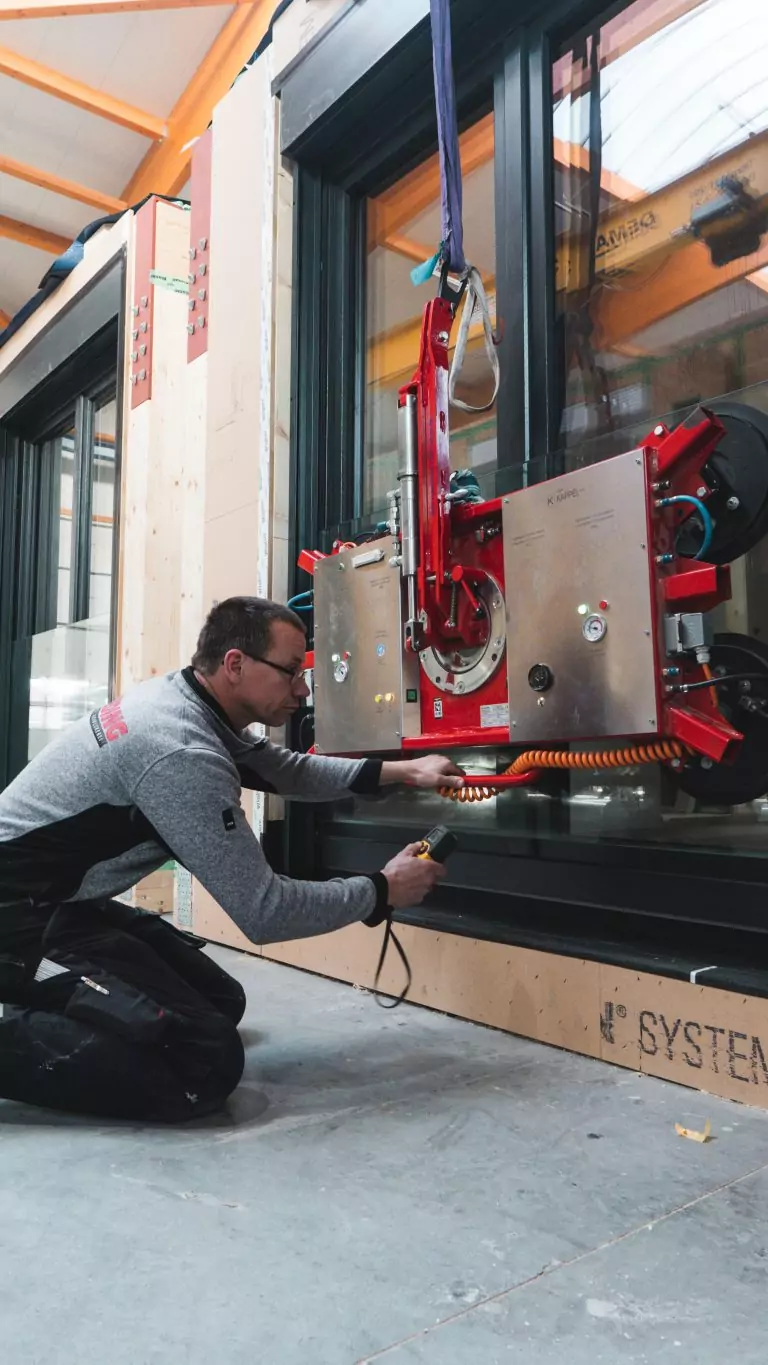 Person arbeitet an einer Glasfassade mit Vakuumheber in einer Werkstatt.