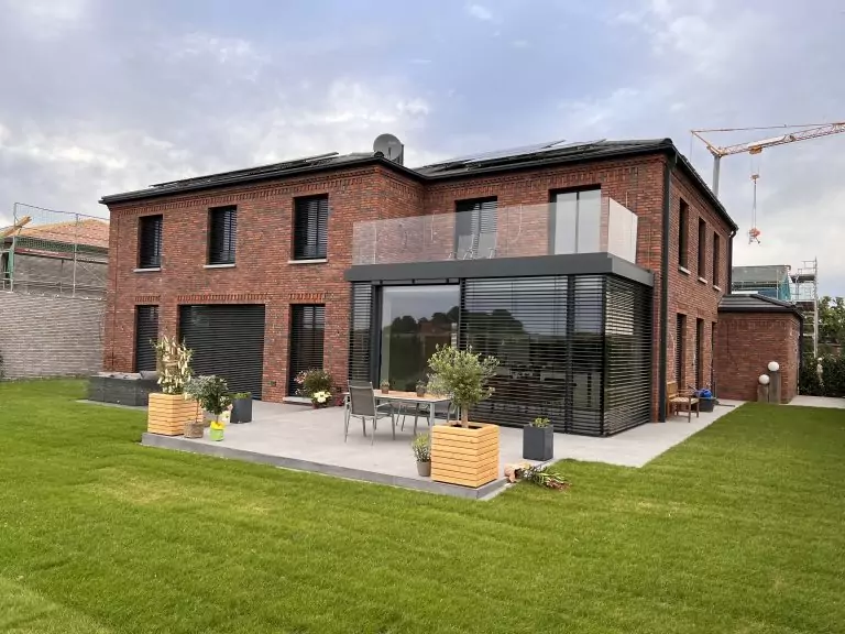 Modernes Backsteinhaus mit großer Terrasse und Garten. Im Hintergrund ist ein Baukran sichtbar.