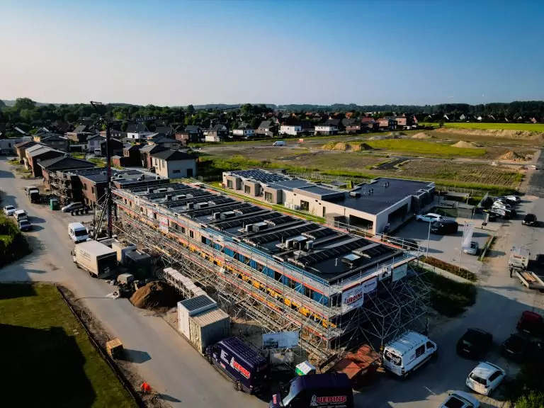 Luftaufnahme einer Baustelle mit Häusern in einem Wohngebiet, Gerüste und Baufahrzeuge sind sichtbar.