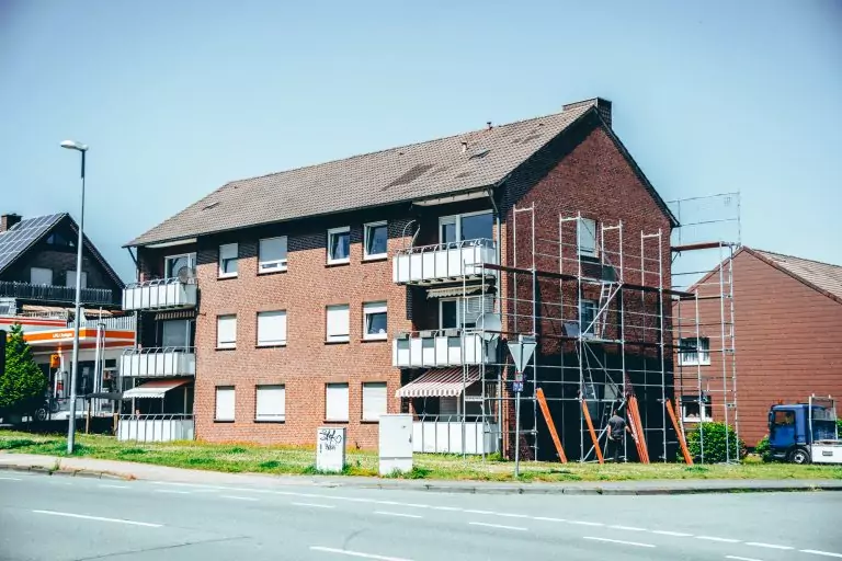 Backsteinwohnhaus mit Gerüst an der Seite, Balkone, daneben eine Straße bei Tageslicht. Vorbereitungen für Bauarbeiten.