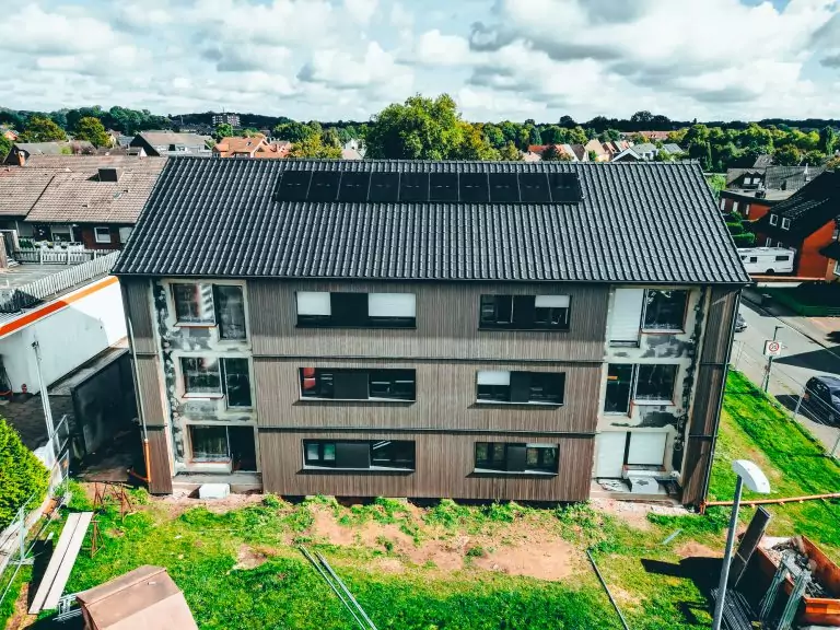 Dreistöckiges Haus mit Solarzellen auf dem Dach in Wohngegend, einige Fenster ohne Verkleidung, grüner Hof.