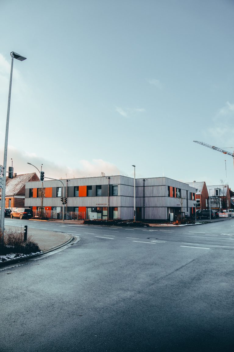 Moderne graue Gebäude mit orangefarbenen Details an einer leeren Straßenkreuzung bei klarem Himmel.